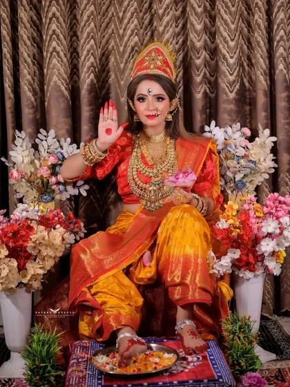 A full-length portrait with the model giving a blessing, surrounded by a vibrant floral setup.