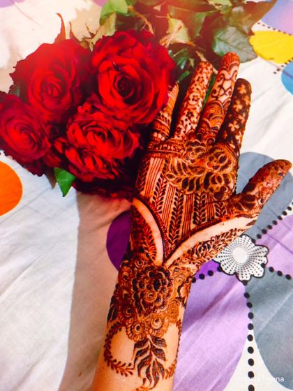 A simple, elegant shot of a beautiful henna stain, held against a bouquet of red roses.