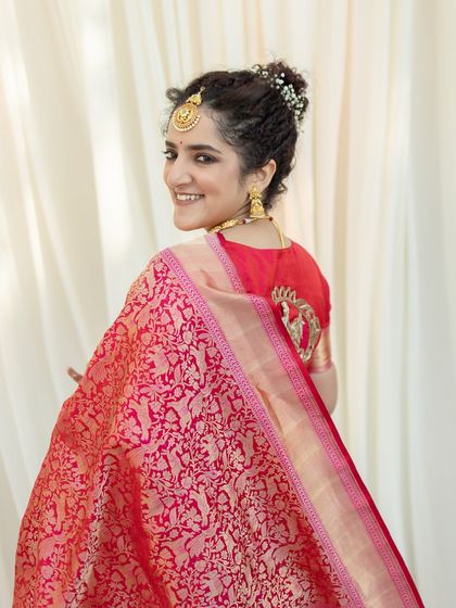 A joyful portrait of a bride in a red Banarasi saree. Her happy glance over her shoulder captures her excitement and radiance on her wedding day.