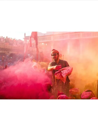 A man throws a bag of pink colored powder into the air during Holi celebrations in Nandgaon. The image captures the explosive energy and joy of the festival.