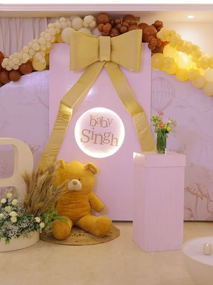 The main backdrop for the "Baby Singh" shower. A large teddy bear sits next to a personalized light-up sign, all framed by a stunning balloon arch in shades of brown, yellow, and cream.
