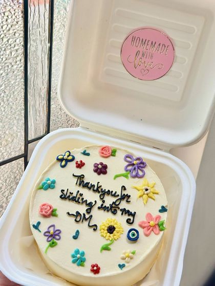 A bento cake celebrating a modern love story that started in the DMs. The tiny, colorful hand-piped flowers add a sweet, romantic touch.