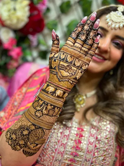 A happy bride showcasing her beautiful back-of-hand mehndi. This design features intricate bands of elephants and paisleys, extending up the arm for a complete and elegant bridal look.
