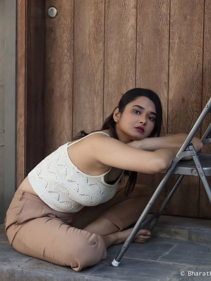 An indoor portrait using a simple chair and a wooden door as a backdrop. The pose is relaxed and has a candid, editorial quality.