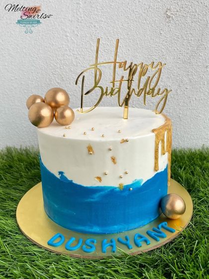 A beautiful blue and white buttercream cake with a touch of gold. The simple design is elevated with gold spheres and a "Happy Birthday" topper.