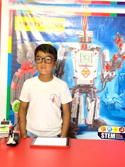 A proud competition winner stands with his programmed LEGO robot, ready to demonstrate its capabilities.