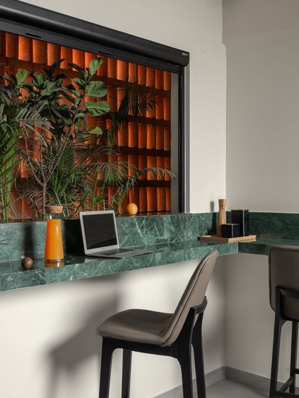 A quiet work nook in our studio, featuring a green marble countertop set against a terracotta jali screen and lush plants. This space is designed to be inspiring and connected to nature.