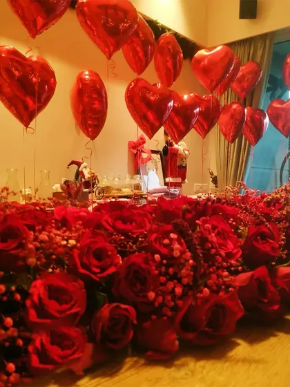 A beautiful tablescape for a Valentine's dinner, combining a dense arrangement of red roses with floating heart balloons.