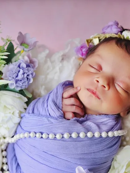 A detailed close-up of a sleeping newborn's face, framed by a floral headband and soft purple flowers. These shots focus on the tiny, perfect features you'll want to remember.