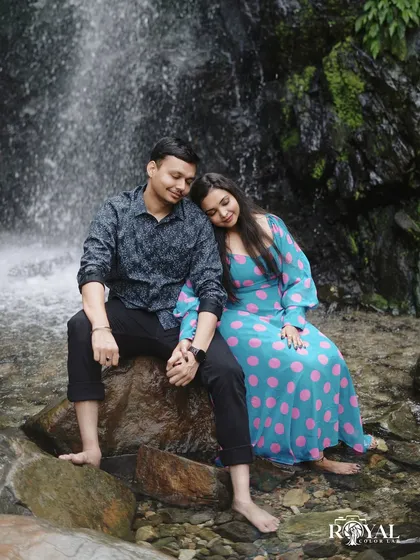 A serene photo of a couple sitting on a rock by a waterfall, holding hands and enjoying the peaceful atmosphere.