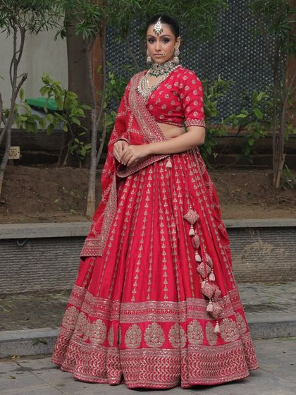 A model looking elegant in a red lehenga, paired with a beautiful Kundan and pearl choker set available for rent.