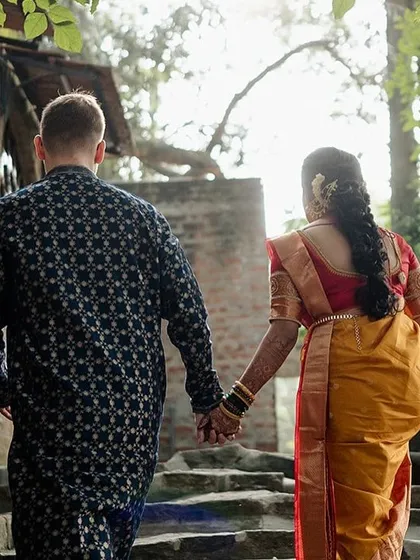 A couple walks hand-in-hand away from the camera, symbolizing their journey forward together, down a path flanked by stone steps and greenery.