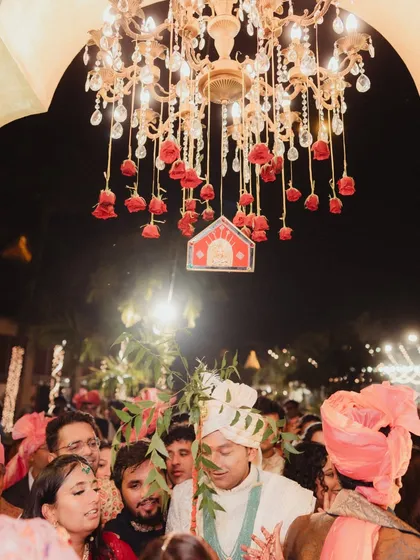 The groom's procession makes its way to the mandap under a chandelier adorned with hanging red roses. This detail adds a touch of romance and luxury to the traditional ceremony.