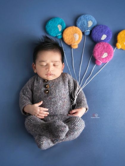 A creative newborn portrait where the baby appears to be floating away with a bunch of colorful felt balloons. This simple yet imaginative setup is done against a solid blue background.