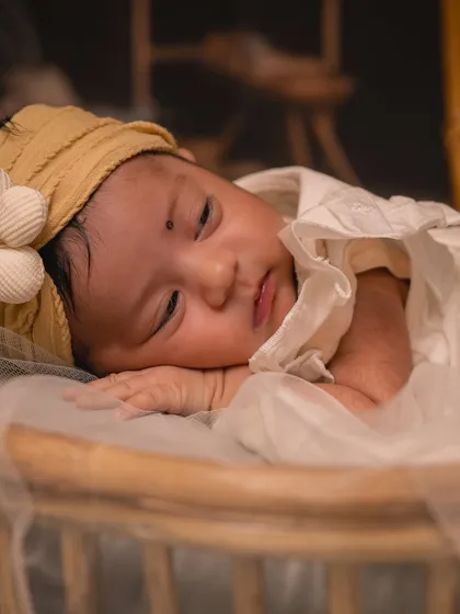 A close-up portrait of a sleeping newborn, peaceful and serene. For these styled infant photos, I use soft fabrics and simple accessories like this floral headband to keep the focus on the baby's delicate features.