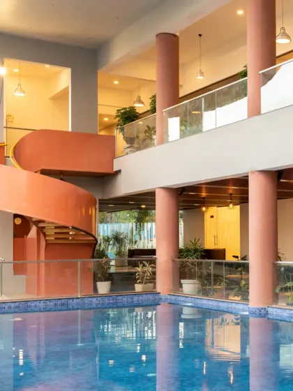 The Sona Vistaas Clubhouse in Bangalore, where a bold, terracotta-red spiral staircase serves as the social and architectural heart of the space. The open, multi-level design encourages interaction, with the swimming pool reflecting the structure and creating a dynamic interplay of light and form.