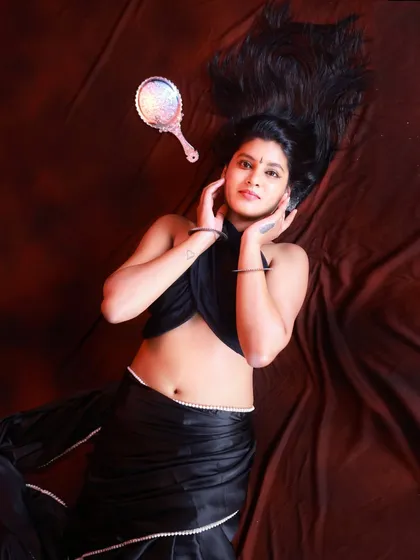 An artistic flat-lay style portrait. The model's hair is fanned out, and the placement of the hand mirror adds a creative element to this studio shot of a modern black saree.