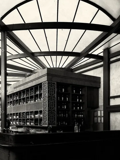 The corner of the bar, showing the detailed fretwork panel and the extensive bottle display. The design combines functionality with decorative, art-deco inspired elements.