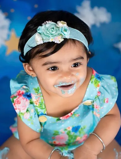A sweet, frosting-covered smile after a fun cake smash. The starry blue background adds a touch of magic to her first birthday photos.