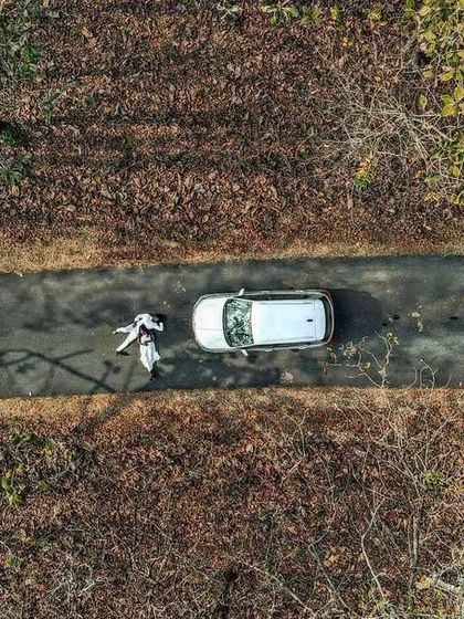 A top-down drone shot of a couple next to their car on a forest road. This image tells a story of a journey and adventure, using the natural lines of the road to create a compelling composition.