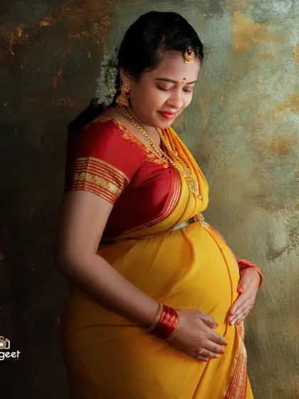 A close-up profile shot focusing on the mother-to-be's serene expression as she cradles her bump. The textured backdrop adds depth to this beautiful saree maternity portrait.