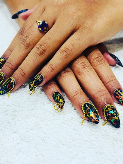 A close-up of these unique glass nails. The design features a dark, shattered glass effect with intricate gold chain piercing on each nail for a bold, edgy look.
