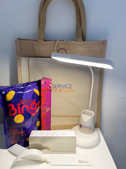 The contents of a birthday hamper for a Service Nextgen employee, including a branded tote bag, desk lamp, and treats. It’s a practical gift they can use every day.