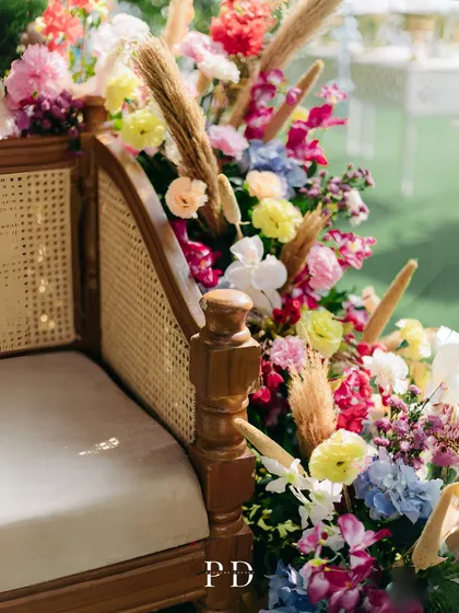 A detail of the stunning floral arrangement on the Mehendi seating, featuring a vibrant mix of roses, hydrangeas, and pampas grass against a rattan sofa.