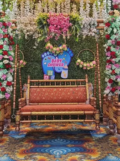 This gender reveal decoration features a lush green backdrop that makes the floral colors pop. The setup includes a central swing, Radha-Krishna cutouts, and 'It's a Boy/Girl' signs, perfect for a vibrant Dohale Jevan.
