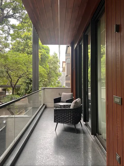 This balcony is designed as a private outdoor retreat. The space features comfortable seating, a wood-paneled soffit that adds warmth, and a glass railing that ensures an unobstructed view of the surrounding greenery.