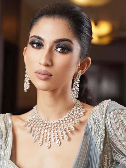 A close-up of a glamorous reception look. The makeup features a classic smokey eye and a nude lip, paired with a stunning diamond and ruby necklace.