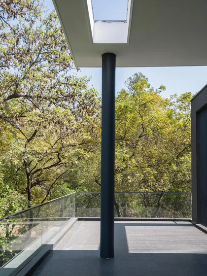 A balcony at Triveni Farmhouse that feels like a treehouse. A simple column supports the roof, which has a cutout for a skylight, while the view is filled with the lush canopy of surrounding trees.