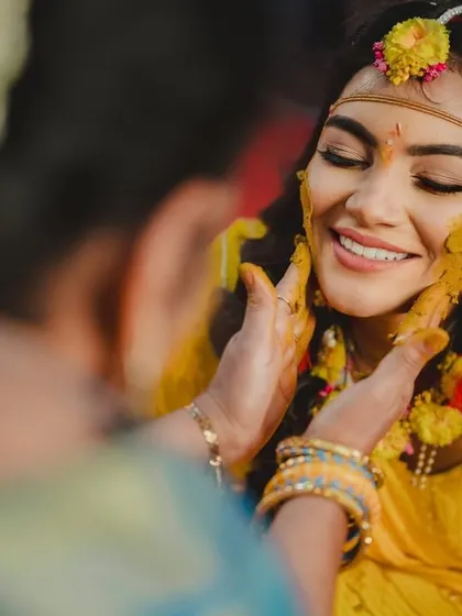 A beautiful close-up of the bride smiling as turmeric paste is applied to her face.