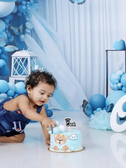The birthday boy reaching for his bear-themed cake in our beautiful blue balloon and butterfly setup.