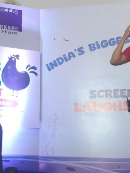 Here I am on stage, wearing a fun character hat and speaking to the audience. We always involve the children in our stories, asking them questions and inviting them to participate, making it an interactive experience for everyone.