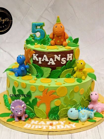 A dino-mite two-tier cake for a 5th birthday. This 4kg chocolate cake is decorated with various colorful fondant dinosaurs and prehistoric foliage for a fun Jurassic adventure.