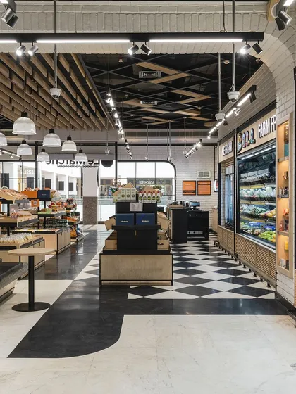 A wide view of the Le Marche interior shows the interplay of different zones. A small seating area offers a place for pause, while the clear sightlines to the beverage and fresh food sections encourage exploration.