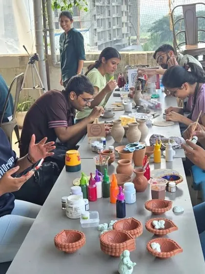 A full table of participants enjoying a painting session. Everyone is focused on their individual pieces, from diyas to vases, in a relaxed, communal setting.