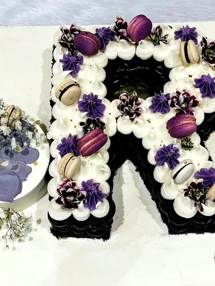 A personalized monogram cake. This "R" shaped cake is decorated with purple and white buttercream swirls and macarons, and comes with a matching mini bento cake.
