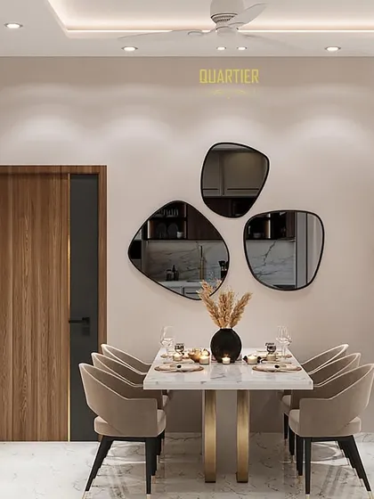 This dining area at Gaur Saundaryam features a wall of abstract-shaped mirrors that act as a piece of art, making the space feel larger and more dynamic. The neutral tones of the furniture create a calm and inviting atmosphere for meals.