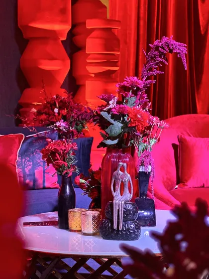 A close-up of a lounge table with unique decor pieces, including a couple's sculpture and geometric vases, all bathed in the Sangeet's signature red glow.