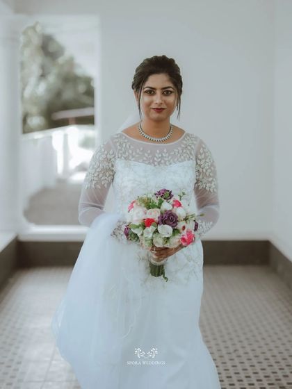 The bride walking towards the camera, holding her bouquet, her white gown flowing gracefully.