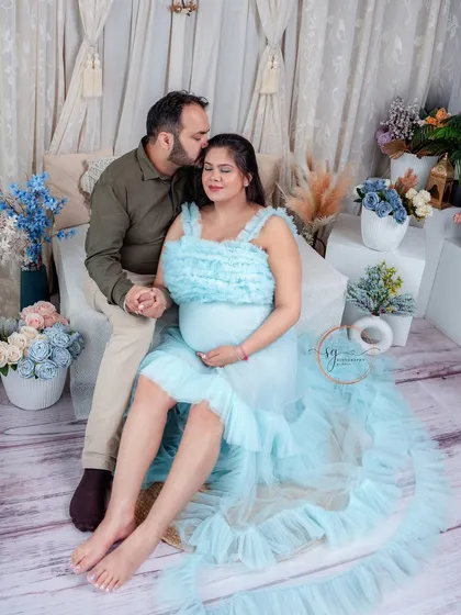 A tender moment captured in a soft, romantic setting. The husband’s gentle kiss on his wife's forehead conveys so much love and care as they await their baby.