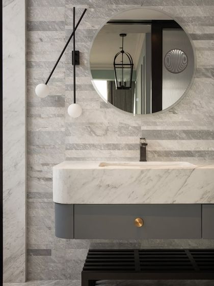 A full view of the Parisian-inspired bathroom. The vanity is set against a backdrop of horizontally stacked marble tiles, with a modern, minimalist light fixture adding a contemporary touch to the classic materials.