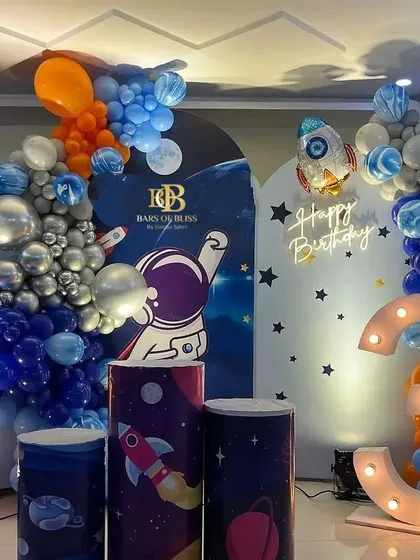 An out-of-this-world space theme for a 3rd birthday. This detailed setup includes multiple backdrops, themed pedestals, a rocket ship balloon, and a large light-up number '3'.