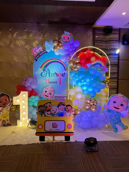 This is a duplicate of ID 1, 68, 226, 184, 190, 213, 240, 250. A vibrant Cocomelon theme for a first birthday party. This setup includes a custom arched backdrop, a rainbow-colored balloon arrangement, and a life-sized cutout of the character JJ.
