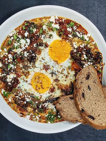 A Middle Eastern Morning: Spinach Simit with Olive Toast: Inspired by a Turkish Simit and a Shakshouka, this breakfast features eggs poached in a savory spinach and tomato base, served with our house-made, high-protein, gluten-free olive bread.