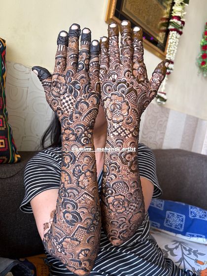 A classic pose showing the full bridal mehendi, with intricate details covering the hands and arms completely.