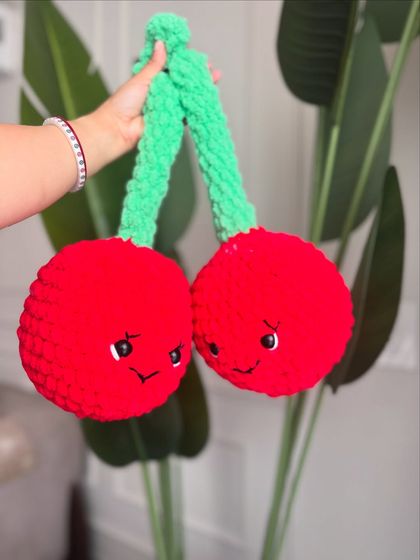 A pair of cherry-red, cheerful plushies. These amigurumi cherries are made with chunky, soft yarn and are perfect as a playful decor item or a cuddly toy.