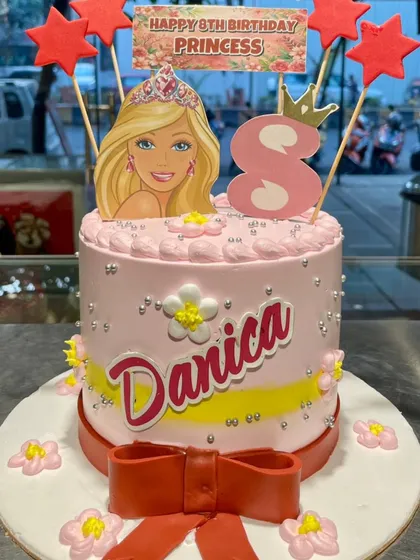 A pretty-in-pink Barbie cake for a princess's 8th birthday. This cake features a Barbie topper, a big red bow, and silver bead details, capturing the glamour and fun of the iconic doll.